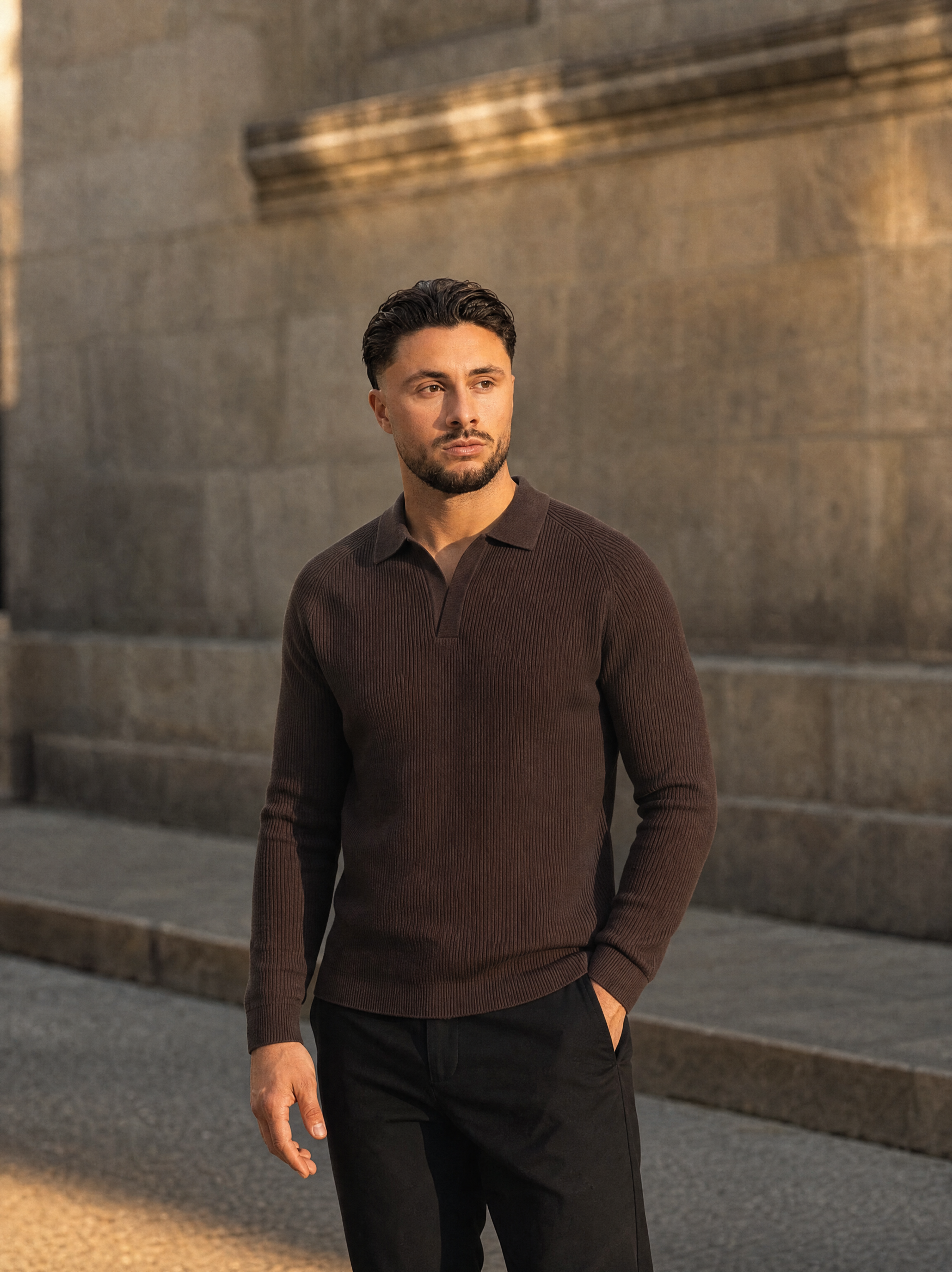 Model in de bruine Ribbed Knit Polo voor een stenen muur